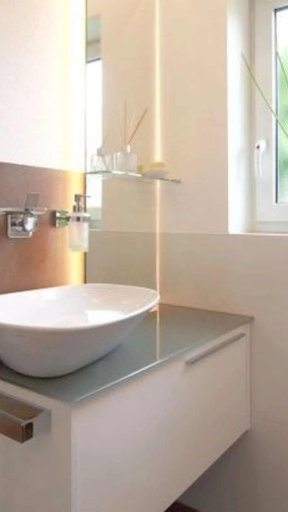 Helles Gäste-WC mit modernem Aufsatzwaschbecken auf weißem Unterschrank, wandmontierter Armatur und dekorativen Details am Fenster.