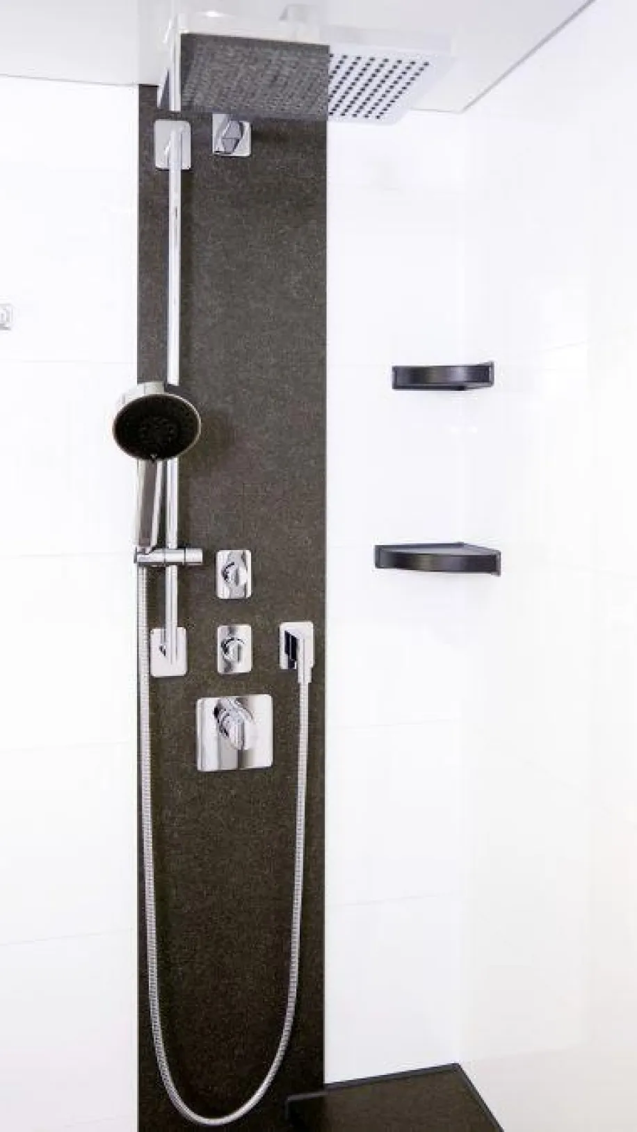 Moderne Dusche mit Regenbrause, Handbrause und verchromten Bedienelementen, eingebaut in eine weiß geflieste Wand mit schwarzem Akzentstreifen und zwei kleinen Eckablagen.