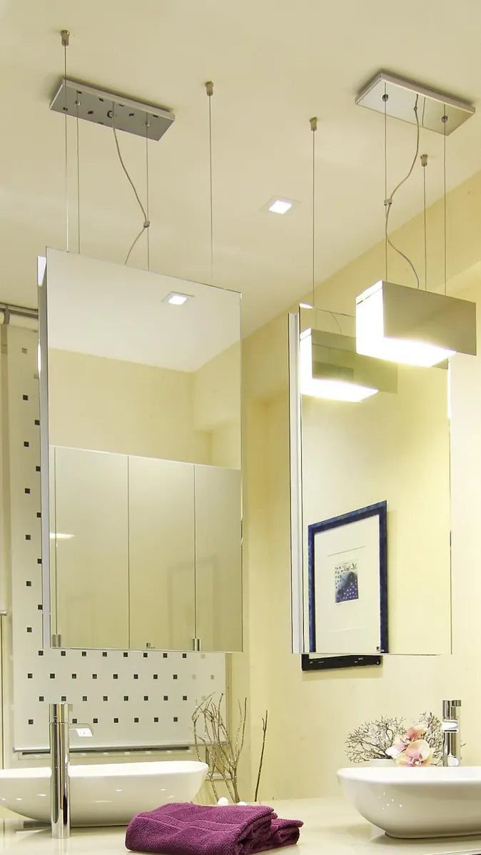Detailaufnahme eines modernen Badezimmers mit hängenden Spiegeln, stilvoller Beleuchtung, zwei Aufsatzwaschbecken und dekorativen Akzenten.