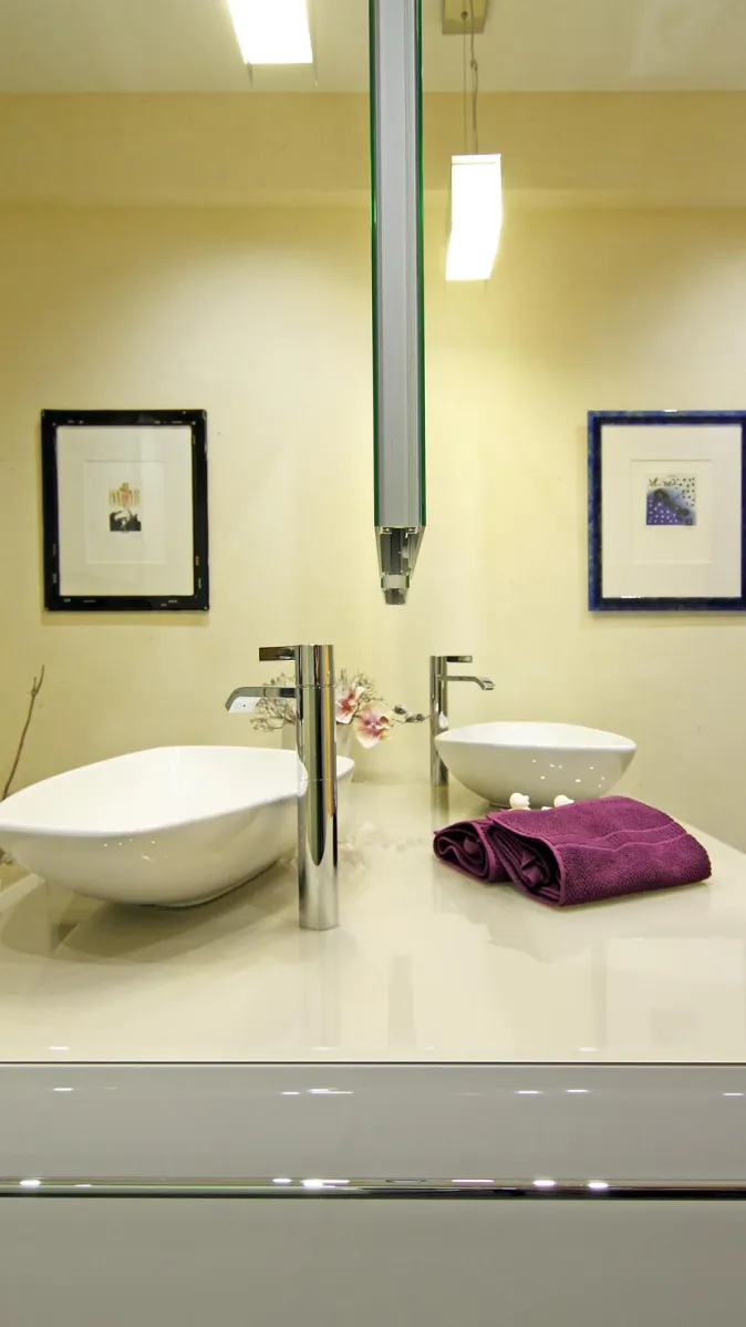 Badezimmer mit modernem Doppelwaschtisch, zwei eleganten Aufsatzwaschbecken, Chromarmaturen, violettem Handtuch und dekorativen Wandbildern.