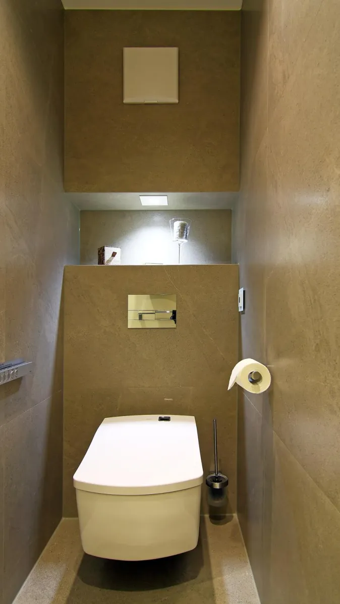 Modernes WC mit wandhängender Toilette, großformatigen Natursteinfliesen, integrierter Ablage mit Beleuchtung und eleganter minimalistischer Gestaltung.