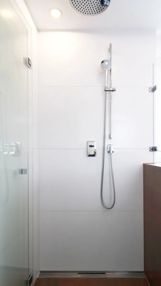 Bodengleiche Dusche mit Glasabtrennung, moderner Regendusche und Handbrause in schlicht-weißem Design.