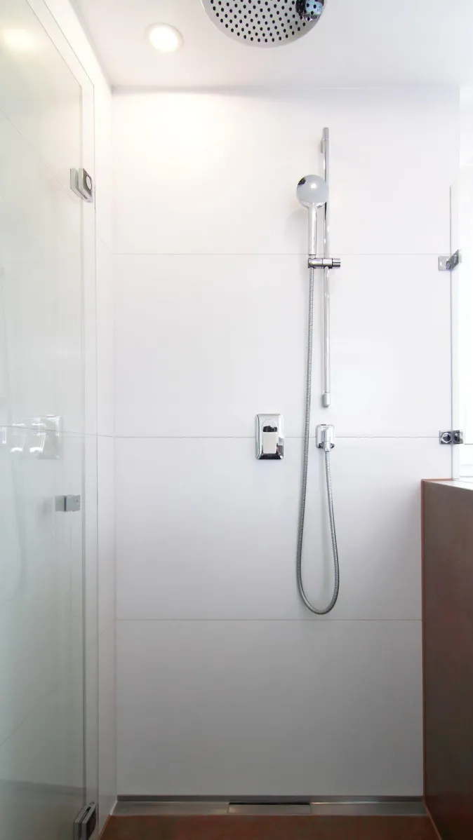 Bodengleiche Dusche mit Glasabtrennung, moderner Regendusche und Handbrause in schlicht-weißem Design.