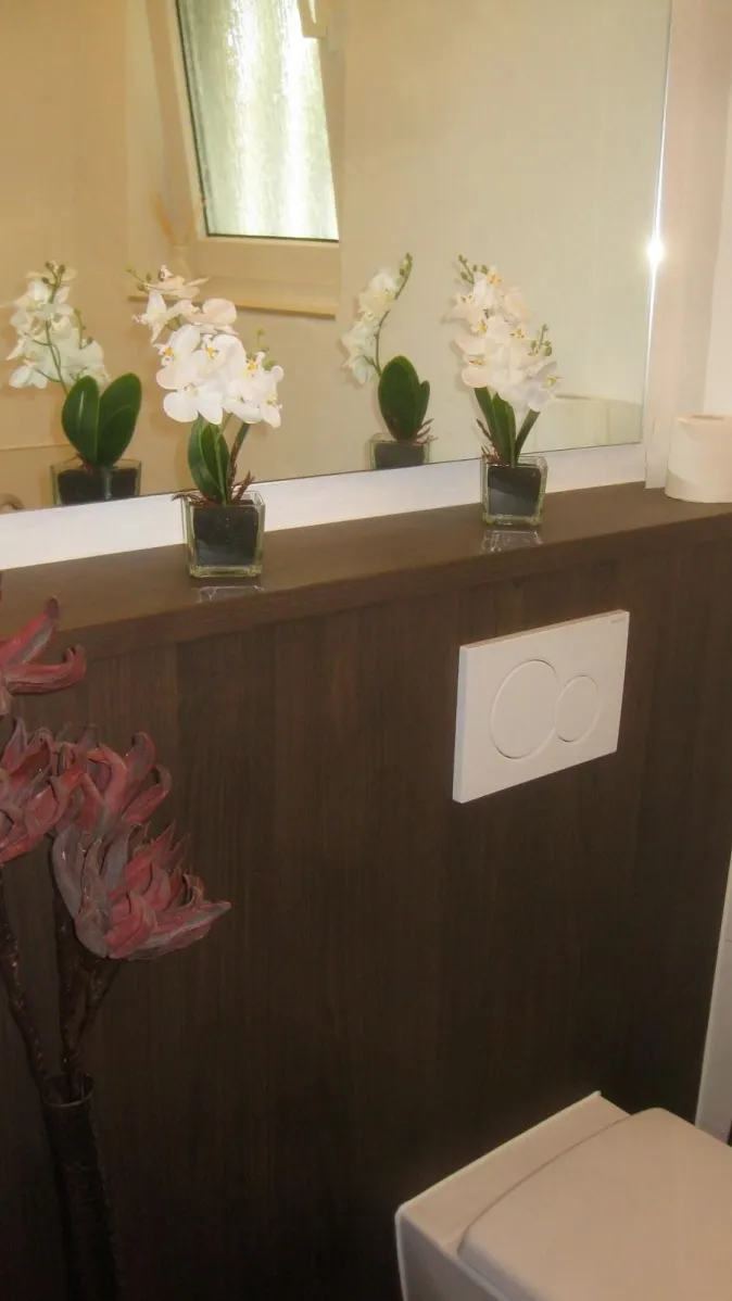 Modernes Gäste-WC mit Holzverkleidung, dekorativen Orchideen auf der Ablage vor dem Spiegel und stilvollen Accessoires.