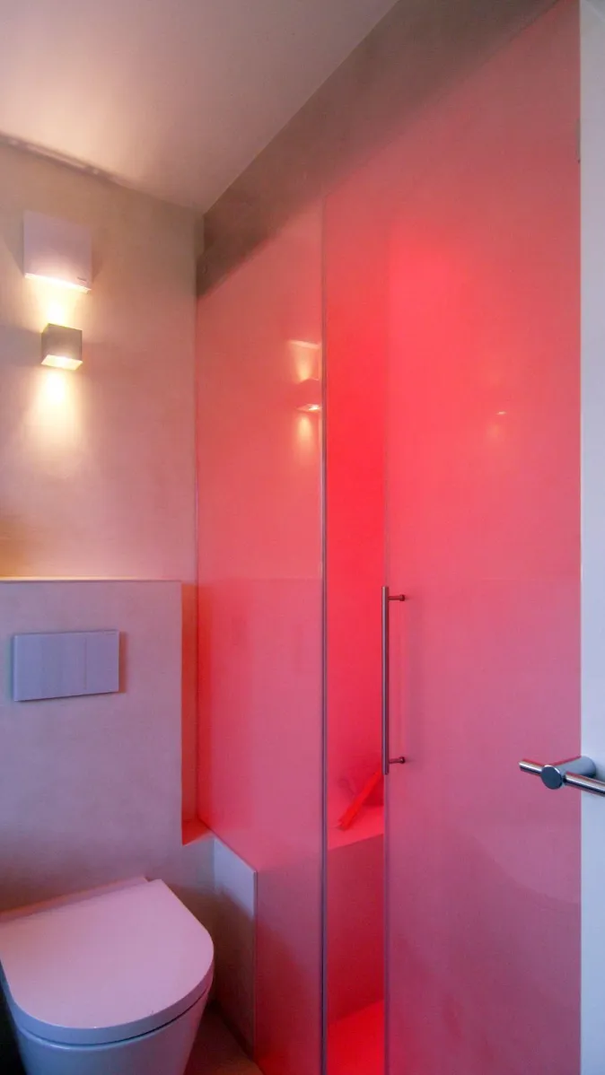 Modernes Badezimmer mit wandhängendem WC und Dampfdusche mit Glasabtrennung sowie LED-Beleuchtung in Rot.