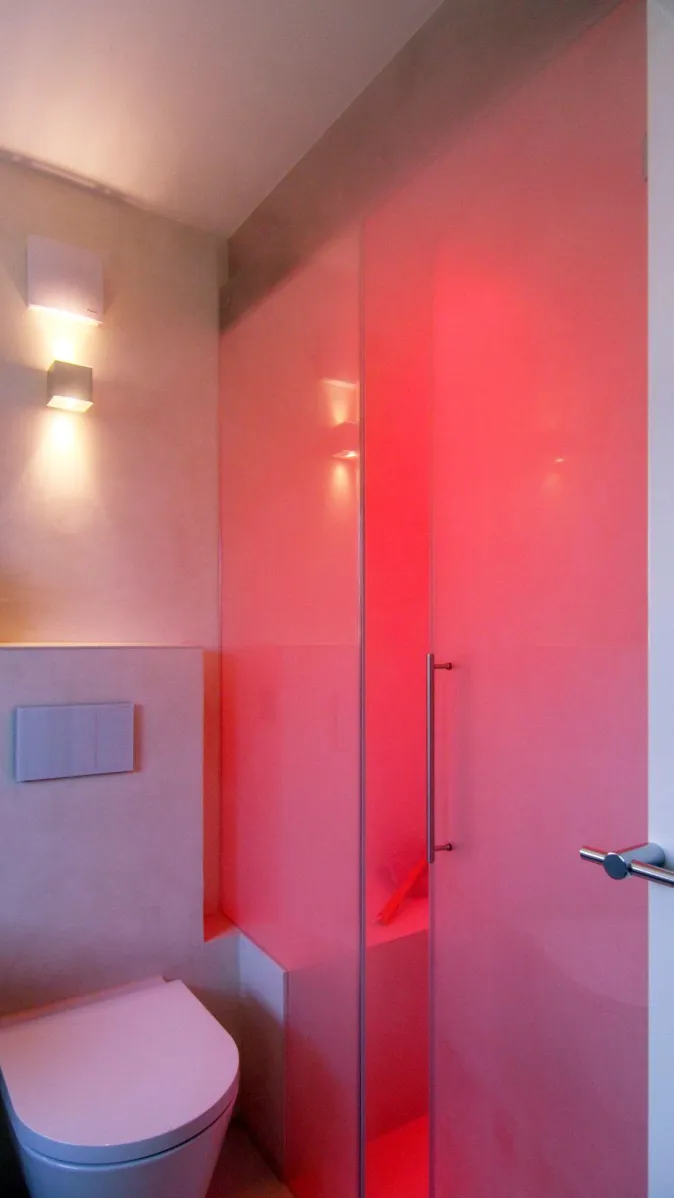 Modernes Badezimmer mit wandhängendem WC und Dampfdusche mit Glasabtrennung sowie LED-Beleuchtung in Rot.
