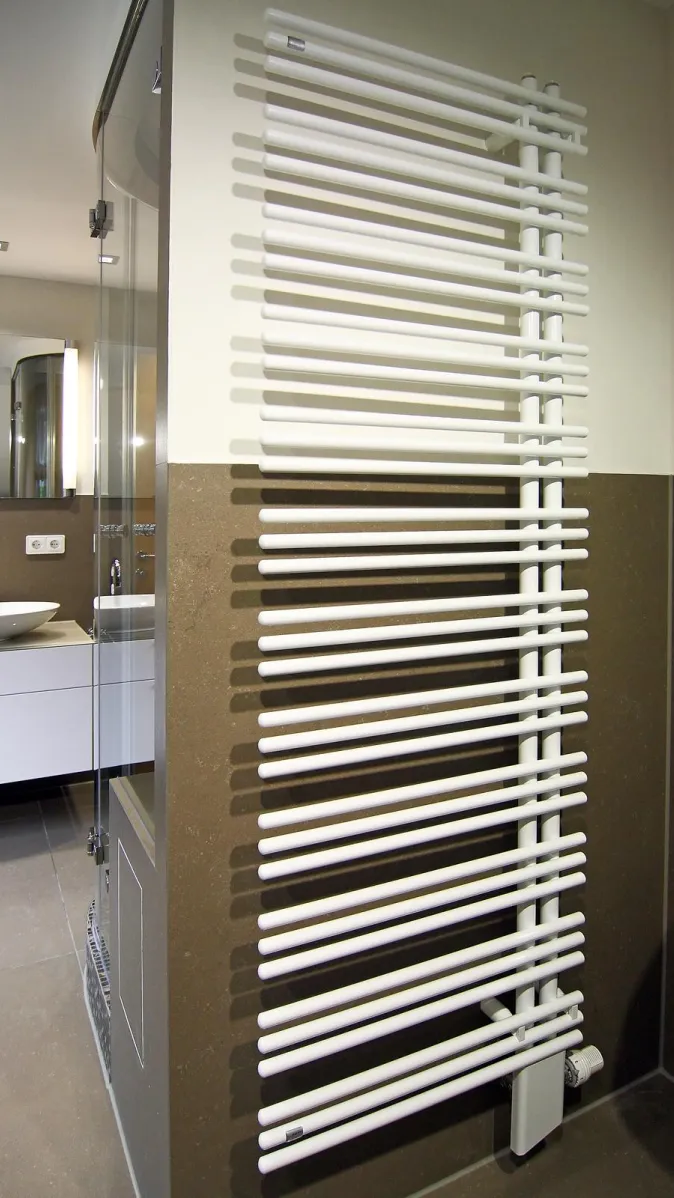 Moderner Design-Heizkörper in einem stilvollen Dampfbad mit Glasdusche und Doppelwaschtisch im Hintergrund.