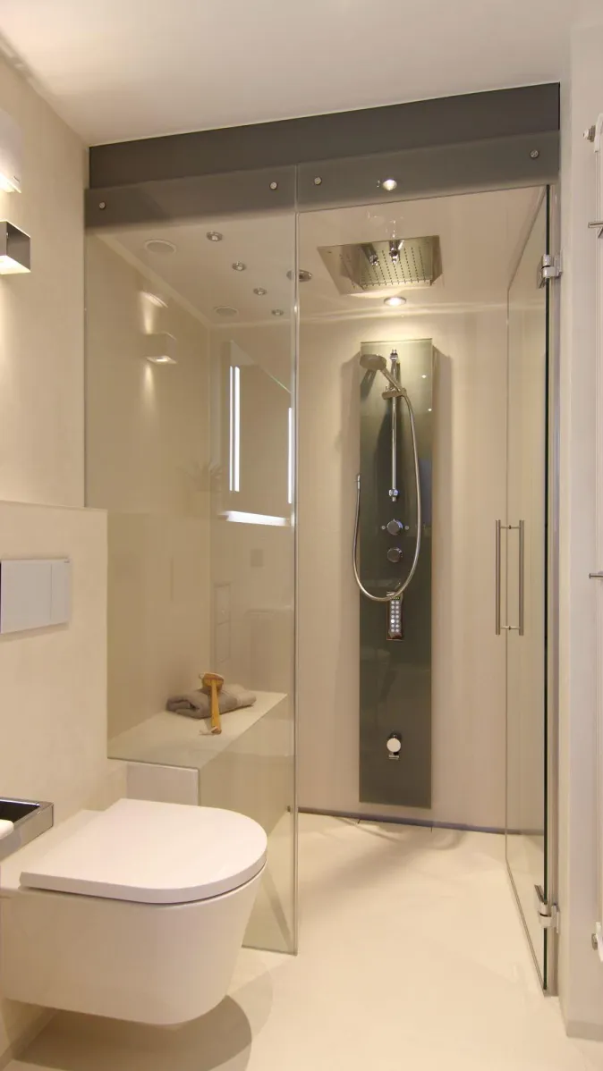 Modernes Dampfbad mit wandhängendem WC, Glasdusche, integrierten Deckenstrahlern und Regenduschkopf im minimalistischen Design.