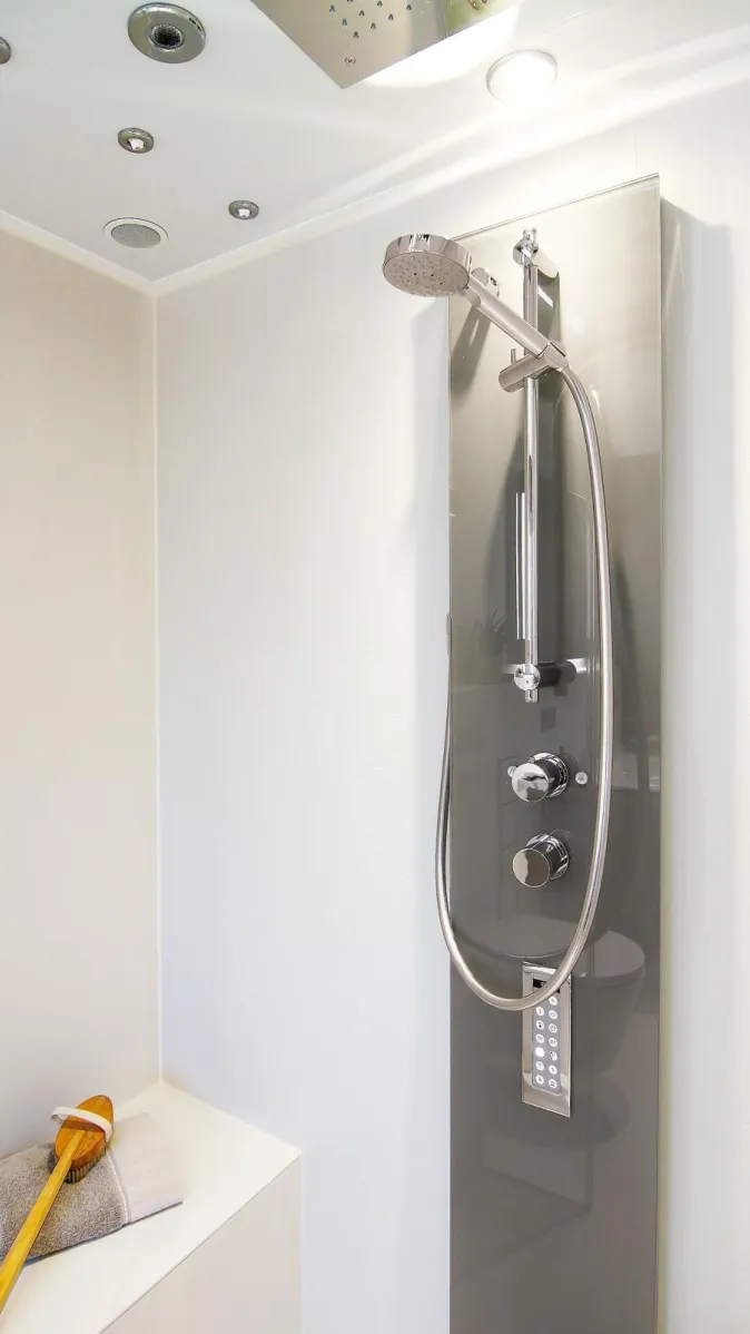 Detailaufnahme einer modernen Dampfdusche mit verchromter Handbrause, Bedienpanel und integrierten Deckenstrahlern.
