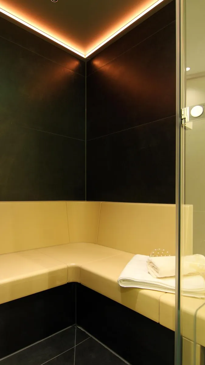 Modernes Dampfbad mit beiger Sitzbank, dunklen Wandfliesen und stimmungsvoller LED-Deckenbeleuchtung.