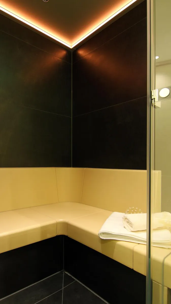 Modernes Dampfbad mit beiger Sitzbank, dunklen Wandfliesen und stimmungsvoller LED-Deckenbeleuchtung.