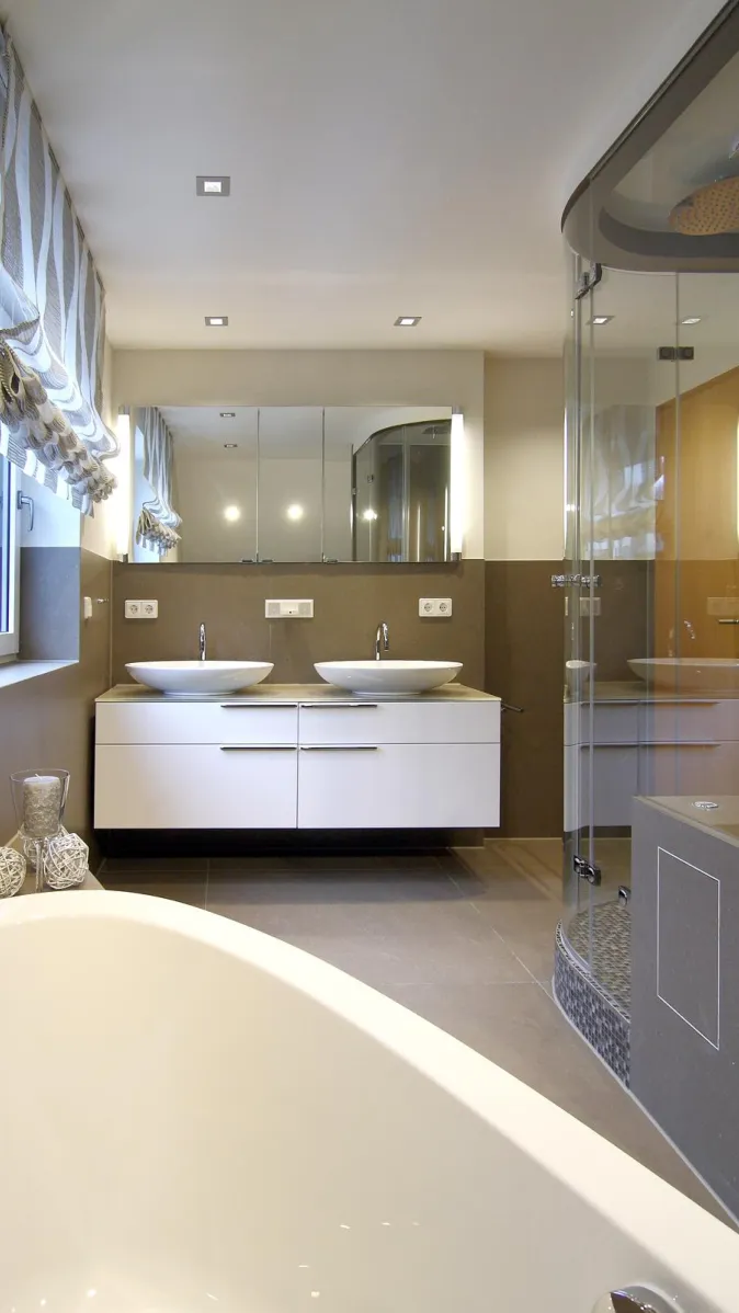 Modernes Dampfbad mit Doppelwaschtisch in Weiß, Glasdusche und eleganter Badewanne in warmen Farbtönen.