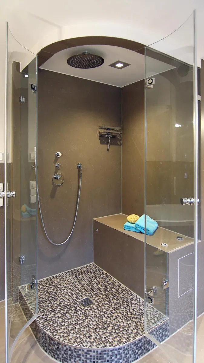 Moderne Dampfdusche mit Glasfront, Mosaikboden, Sitzbank und Regendusche in elegantem Badezimmerdesign.