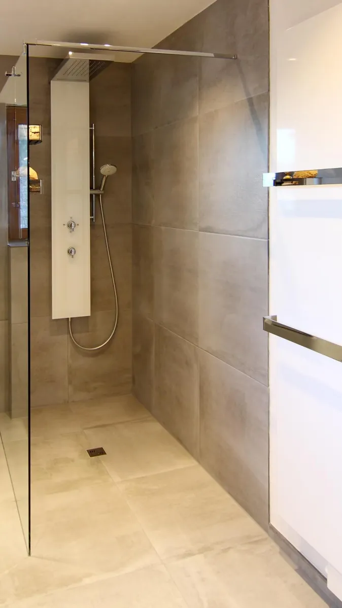 Bodengleiche Dusche mit Glasabtrennung, großformatigen grauen Fliesen und moderner Duscharmatur mit Handbrause.