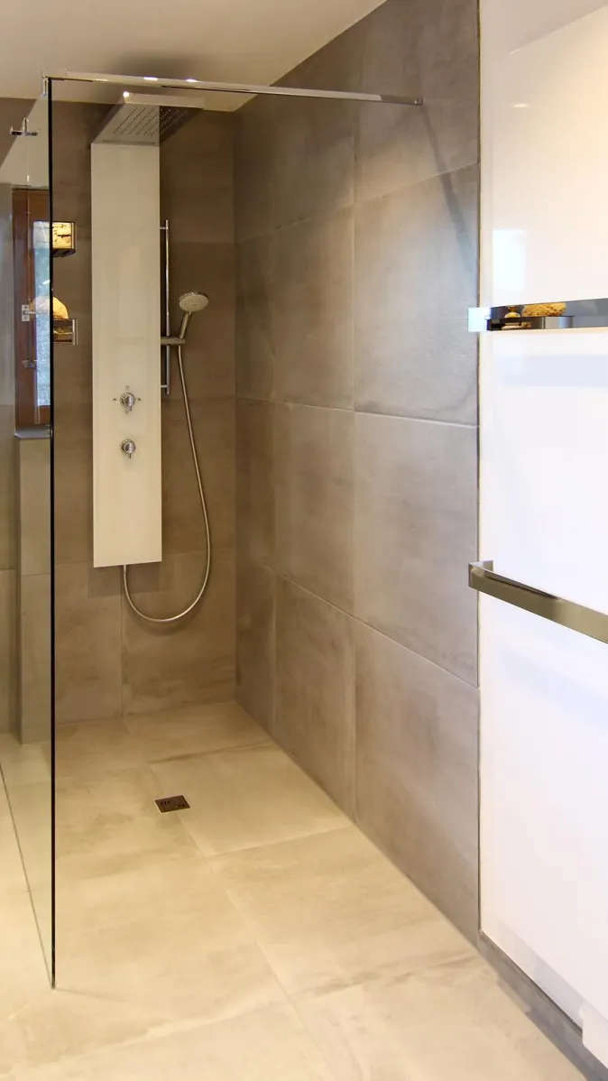 Bodengleiche Dusche mit Glasabtrennung, großformatigen grauen Fliesen und moderner Duscharmatur mit Handbrause.