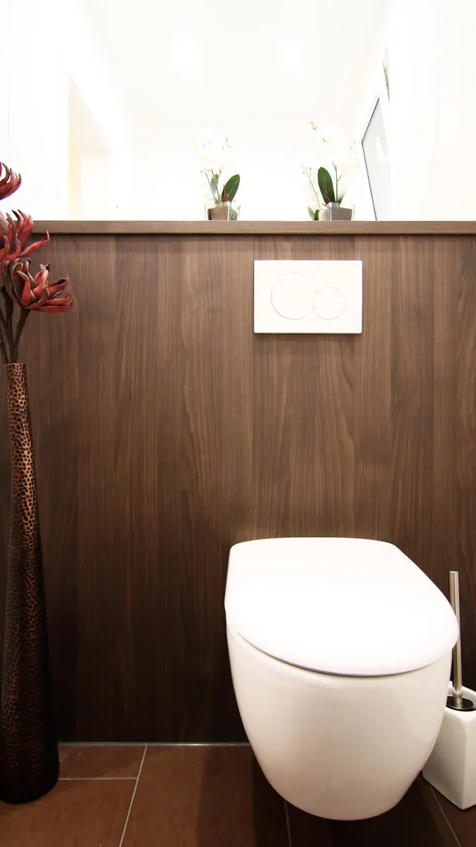 Modernes Gäste-WC mit dunkler Holzverkleidung, wandhängendem WC und dekorativen Pflanzen-Accessoires.