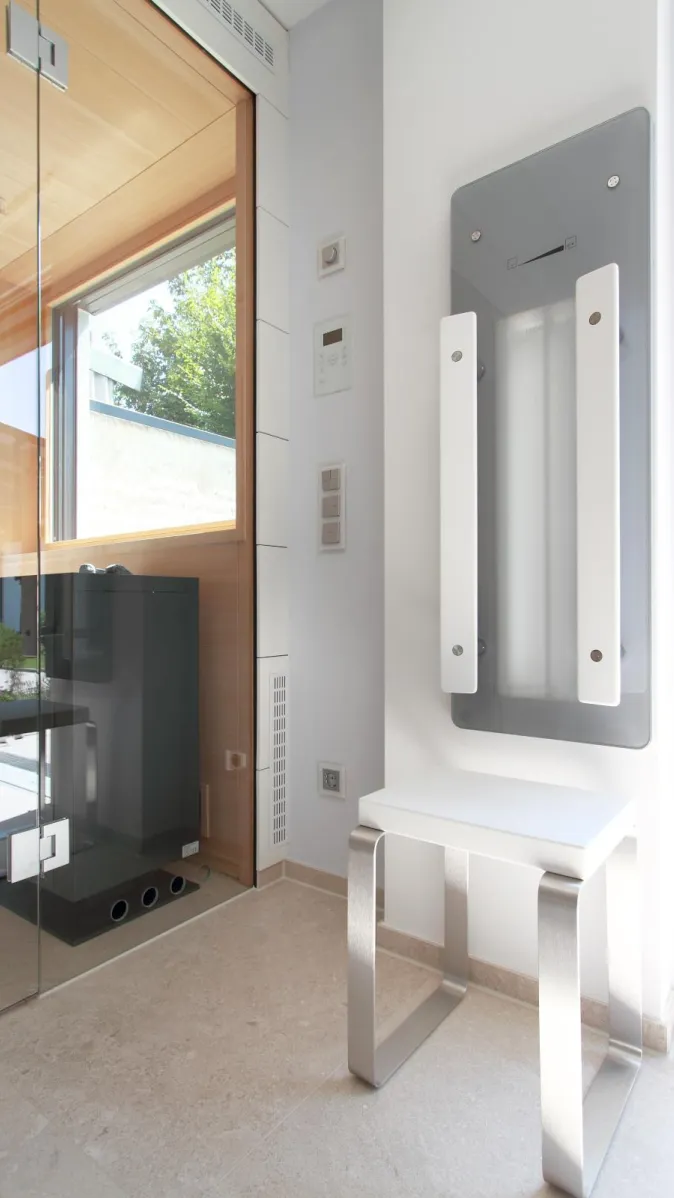 Saunabereich mit Glasabtrennung, moderner Technik und stilvollem Sitzbereich in einem hellen Wellnessbad.