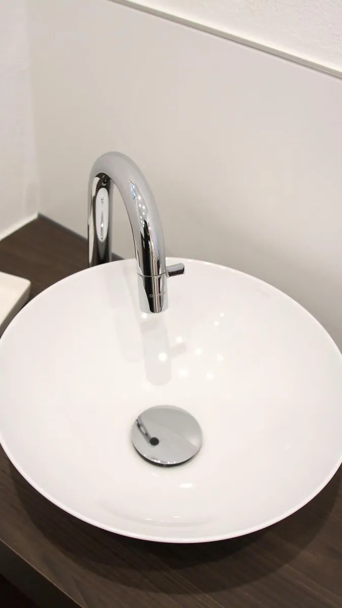 Eleganter Waschtisch im Gäste-WC mit runder weißer Aufsatzschale und moderner verchromter Armatur.