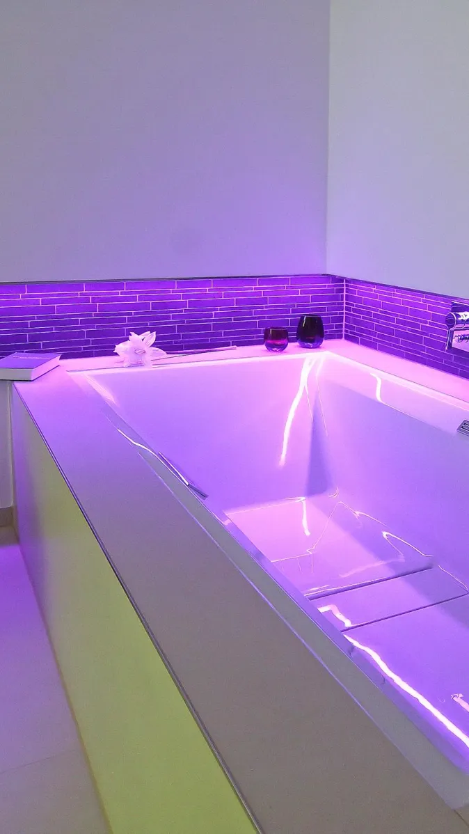 Moderne Badewanne mit stimmungsvoller lila LED-Beleuchtung und violettem Fliesenmosaik an der Wand.