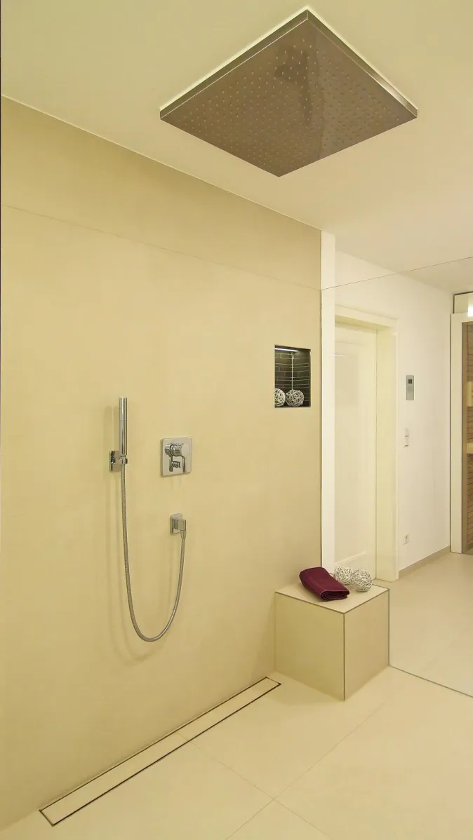Moderne, begehbare Dusche mit großer Regendusche in der Decke, minimalistischer Armatur, integrierter Sitzbank und hellem, puristischem Design.