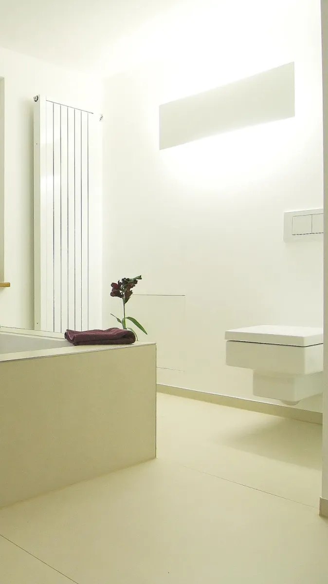Helles, minimalistisches Badezimmer mit moderner Badewanne, wandhängendem WC, weißem Heizkörper und schlichter Dekoration.