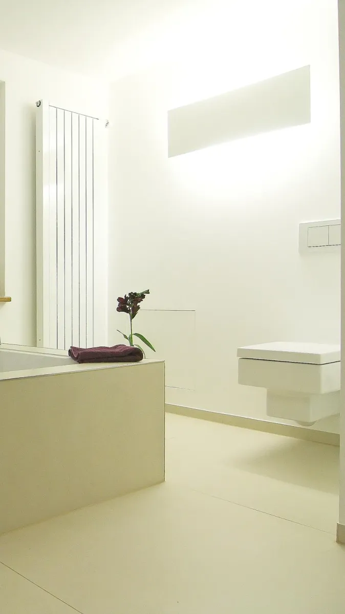 Helles, minimalistisches Badezimmer mit moderner Badewanne, wandhängendem WC, weißem Heizkörper und schlichter Dekoration.