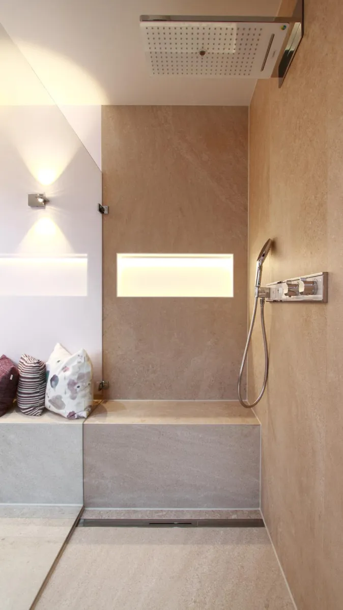 Moderne begehbare Dusche mit Regenduschkopf, Sitzbank, Nischenbeleuchtung und eleganten Steinfliesen im Wohnbad Eislingen Nord.