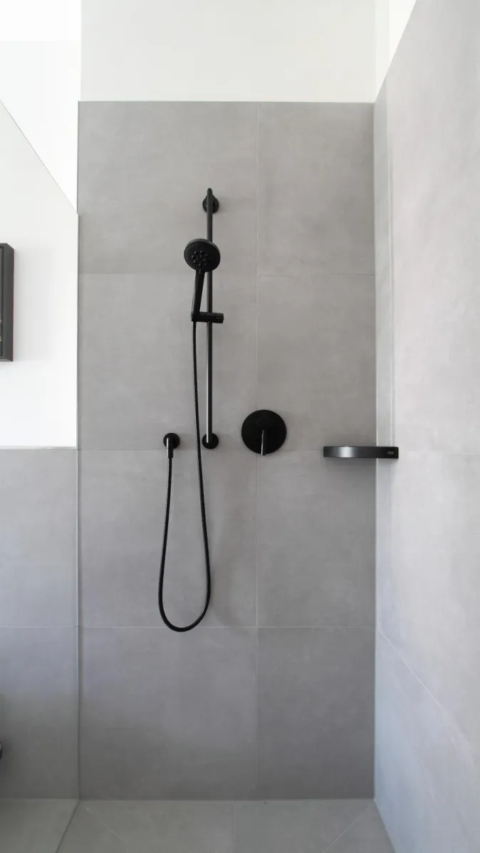 Moderne Dusche in Betonoptik mit grauen Fliesen und schwarzer Armatur.