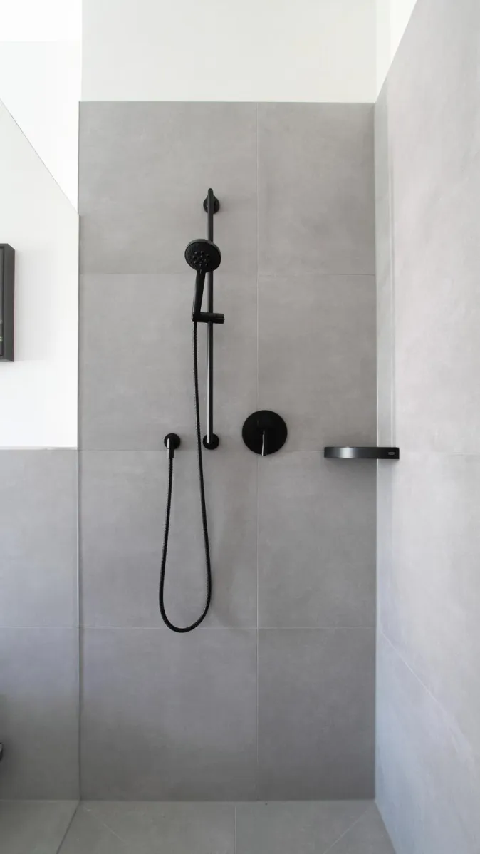 Moderne Dusche in Betonoptik mit grauen Fliesen und schwarzer Armatur.