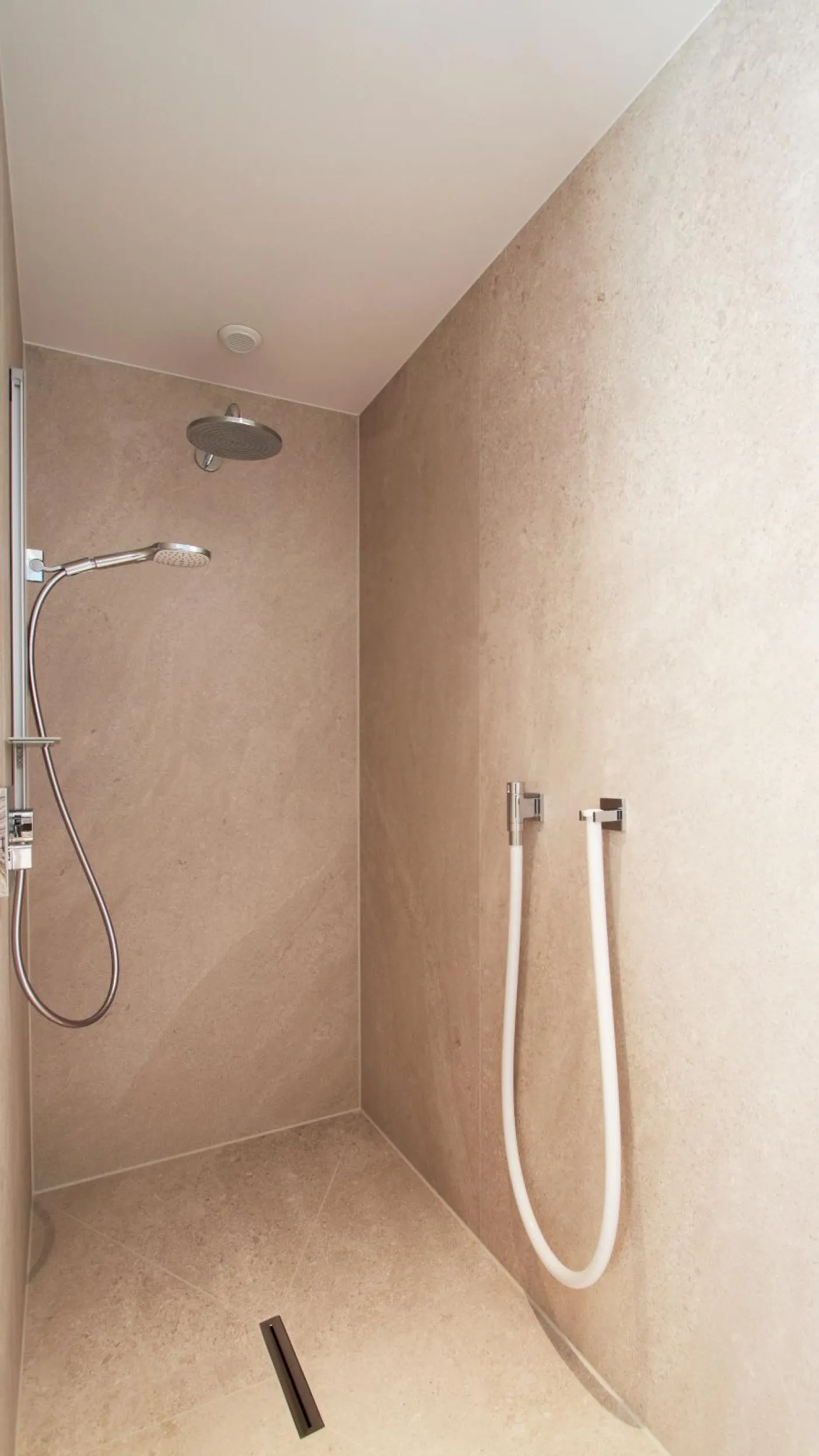Bodenebene Dusche mit Regenbrause und Handbrause in einem modernen Sauna-Wellnessbad mit Natursteinoptik.