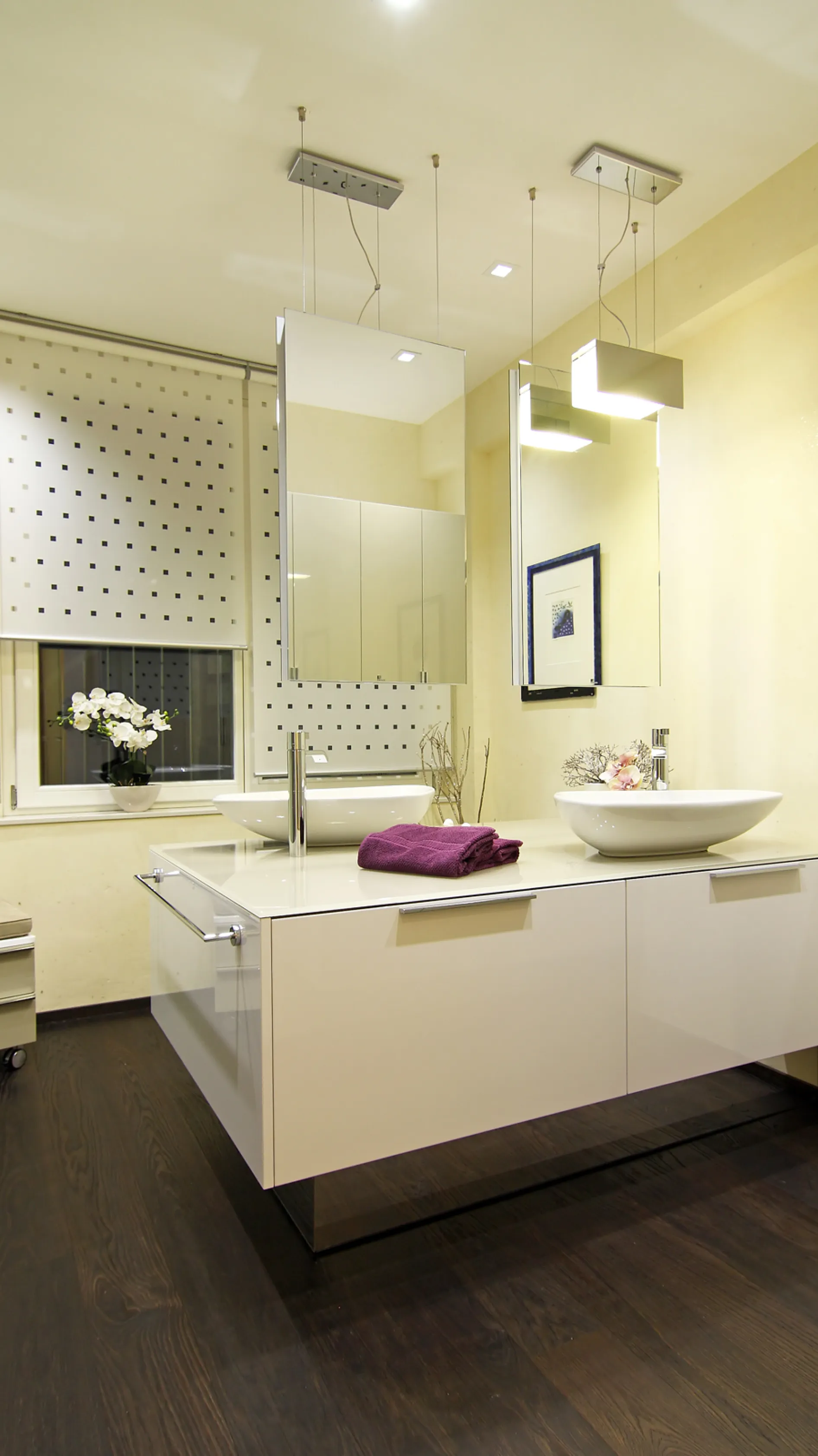 Elegantes Badezimmer mit schwebendem Waschtisch, zwei modernen Aufsatzwaschbecken, stilvoller Spiegelbeleuchtung, Orchidee am Fenster und dekorativen Akzenten.
