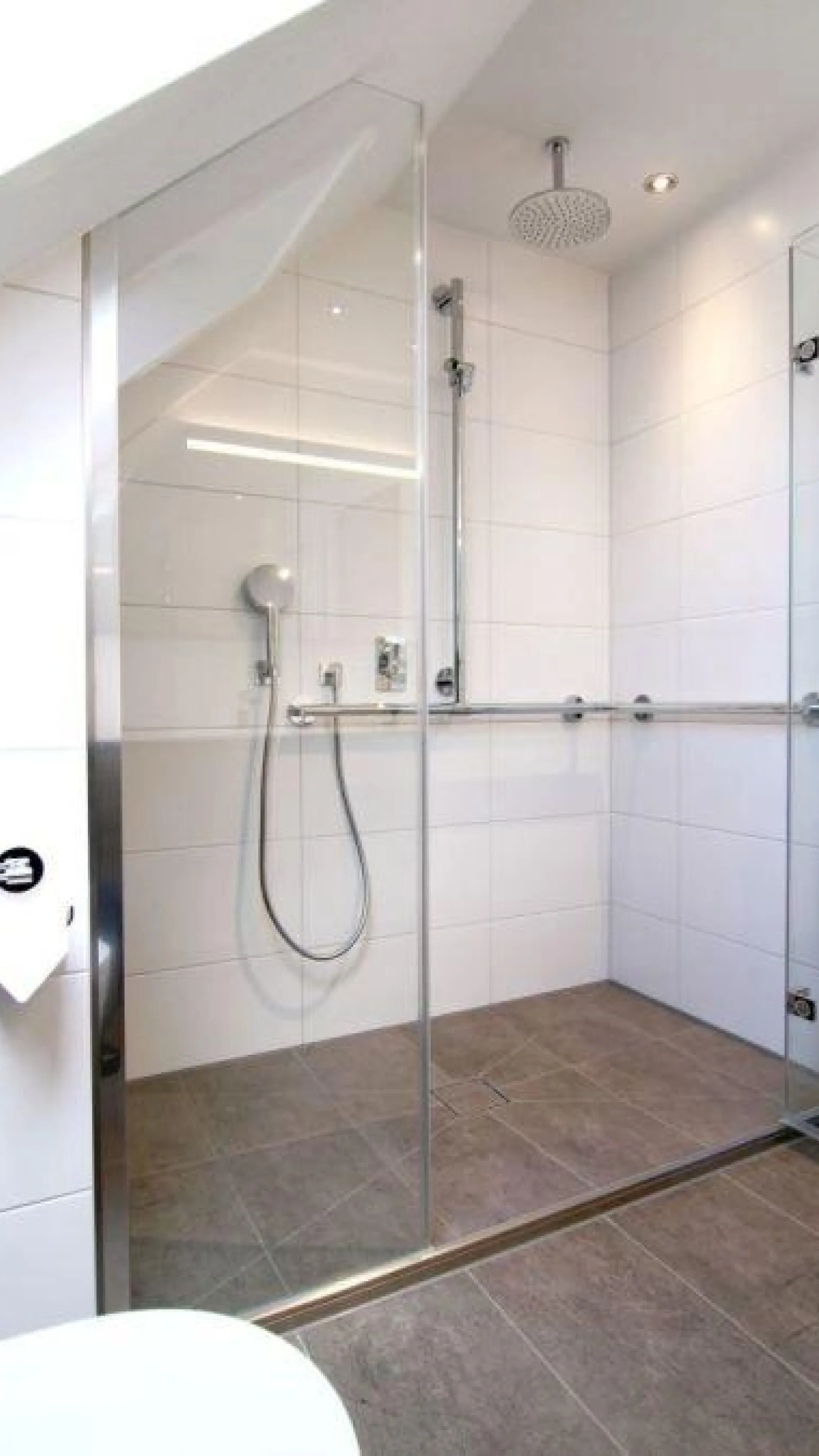 Bodengleiche, barrierefreie Dusche im altersgerechten Dachbad mit Glasabtrennung, Haltegriff und moderner Regendusche.