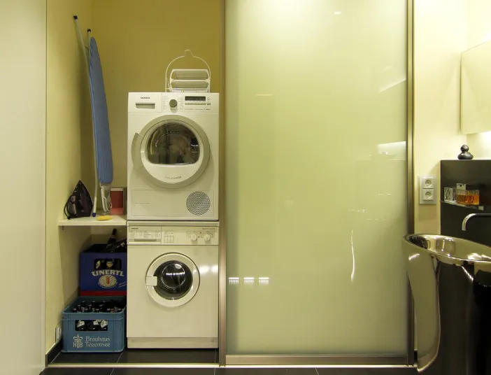 Gästebad mit integriertem Hauswirtschaftsbereich: Waschmaschine und Trockner in Nische mit Bügelbrett, daneben eleganter Edelstahl-Waschtisch.