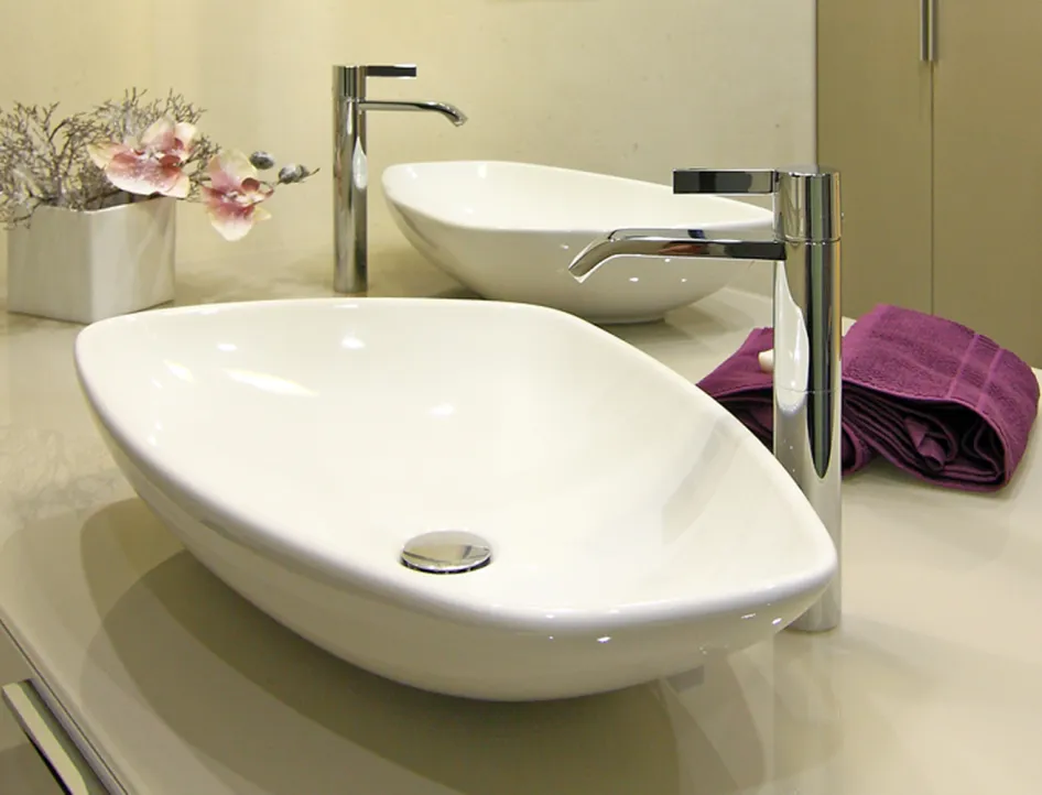 Nahaufnahme eines eleganten Aufsatzwaschbeckens mit moderner Chromarmatur, dekorativer Orchidee und violettem Handtuch auf einem glänzenden Waschtisch.