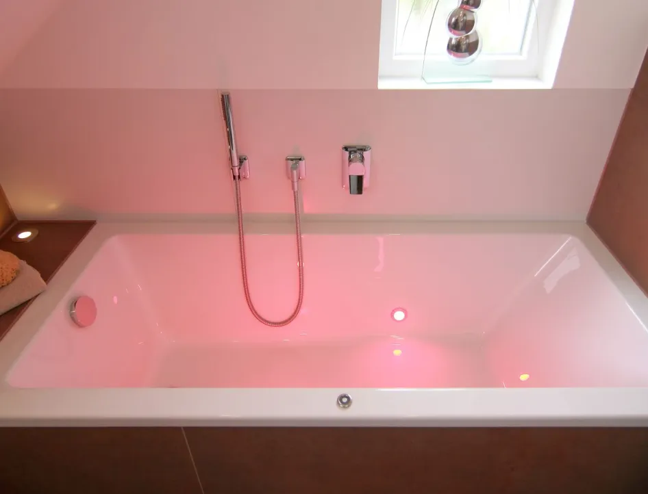 Moderne Badewanne mit integrierter LED-Farbbeleuchtung in Rot, Wandarmaturen und dekorativen Accessoires am Wannenrand.