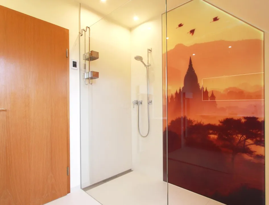 Bodenebene Dusche mit Glasabtrennung, moderner Handbrause und großflächigem Wandmotiv in warmen Orange- und Rottönen, das eine Landschaft mit Tempelsilhouette zeigt.