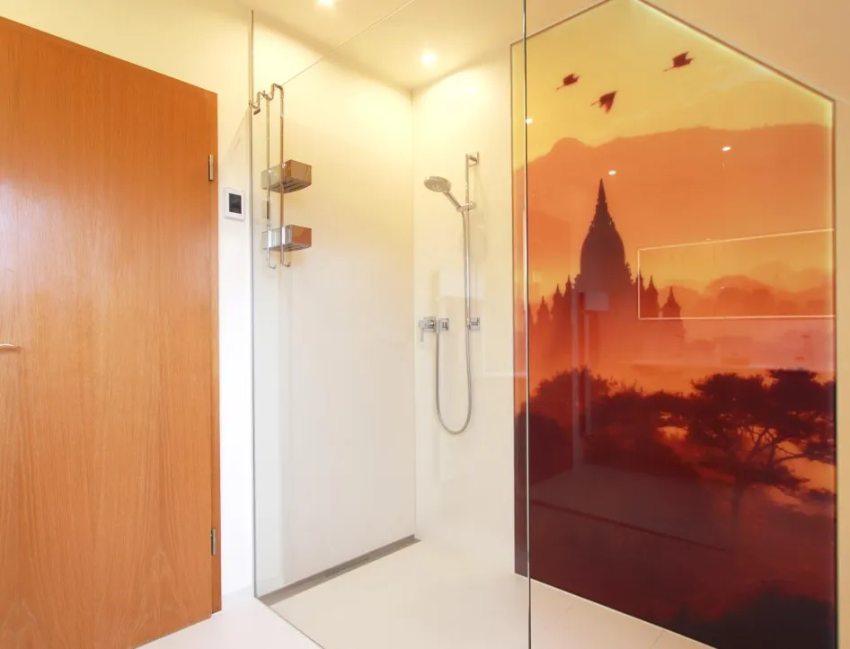 Bodenebene Dusche mit Glasabtrennung, moderner Handbrause und großflächigem Wandmotiv in warmen Orange- und Rottönen, das eine Landschaft mit Tempelsilhouette zeigt.