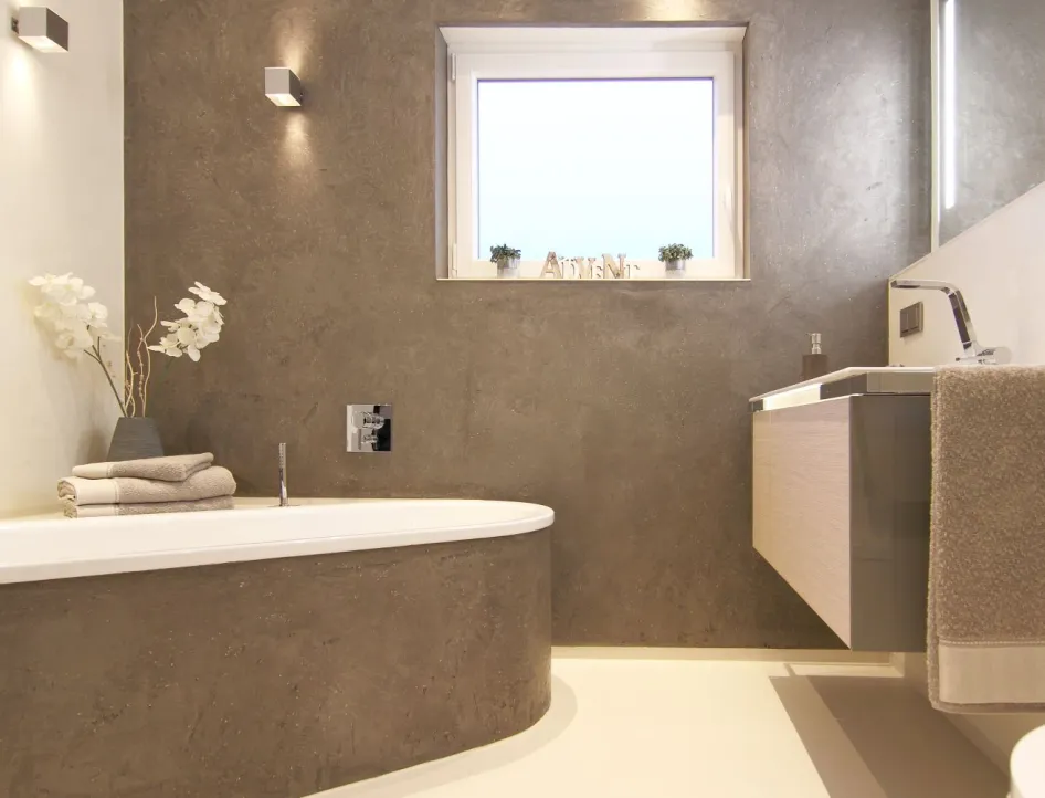 Modernes Badezimmer mit grauer Steinwand, eingebauter Badewanne, Holzwaschtisch und minimalistischer Dekoration mit Handtüchern und weißen Orchideen.