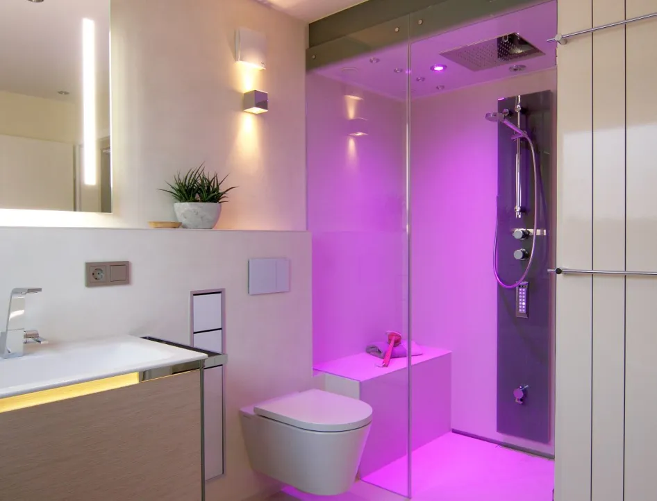 Modernes Badezimmer mit Waschtisch, wandhängendem WC und Dampfdusche mit LED-Farbbeleuchtung in kräftigem Violett.