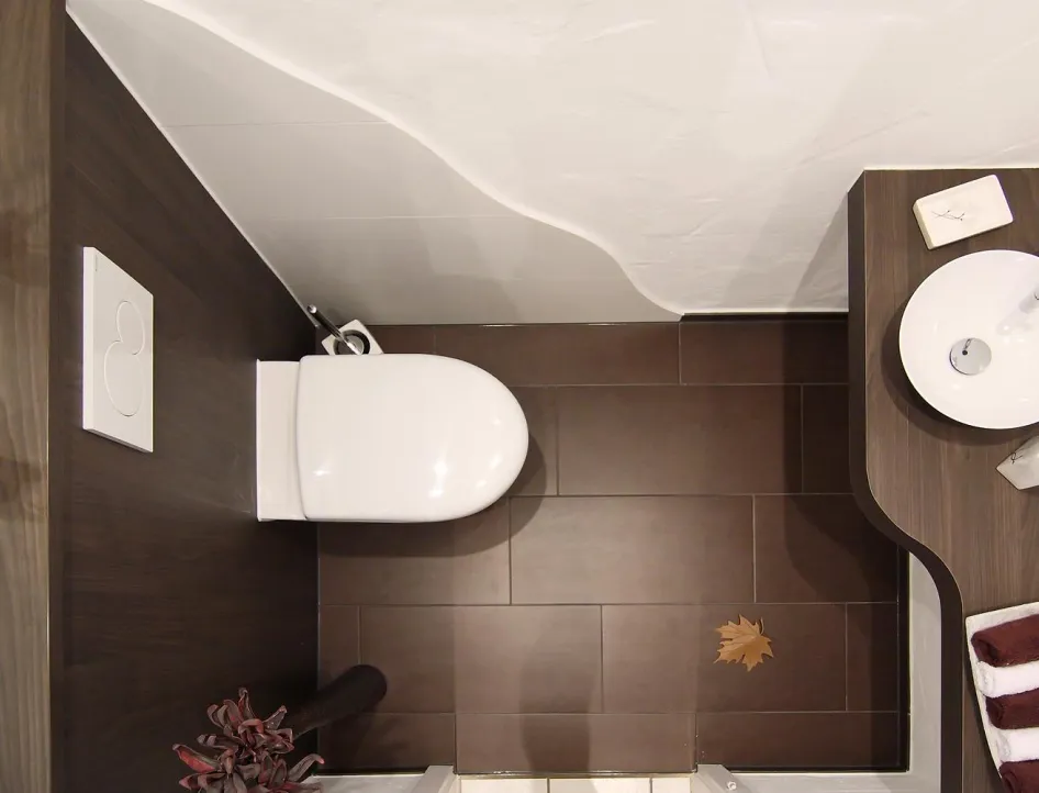 Modernes Gästebad in Vogelperspektive mit weißem WC, rundem Aufsatzwaschbecken auf dunkler Holzablage und dekorativen Handtüchern.
