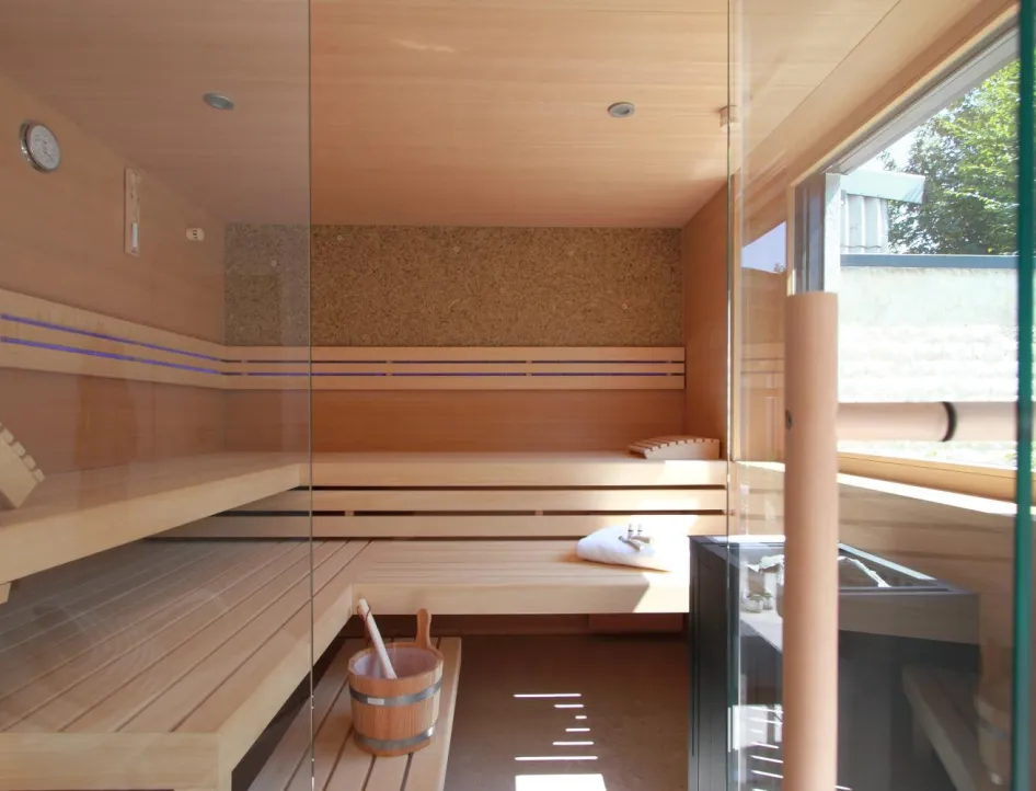 Großzügige Privatsauna mit Holzvertäfelung, Glasfront und gemütlichen Liegebänken, durchflutet von Tageslicht.