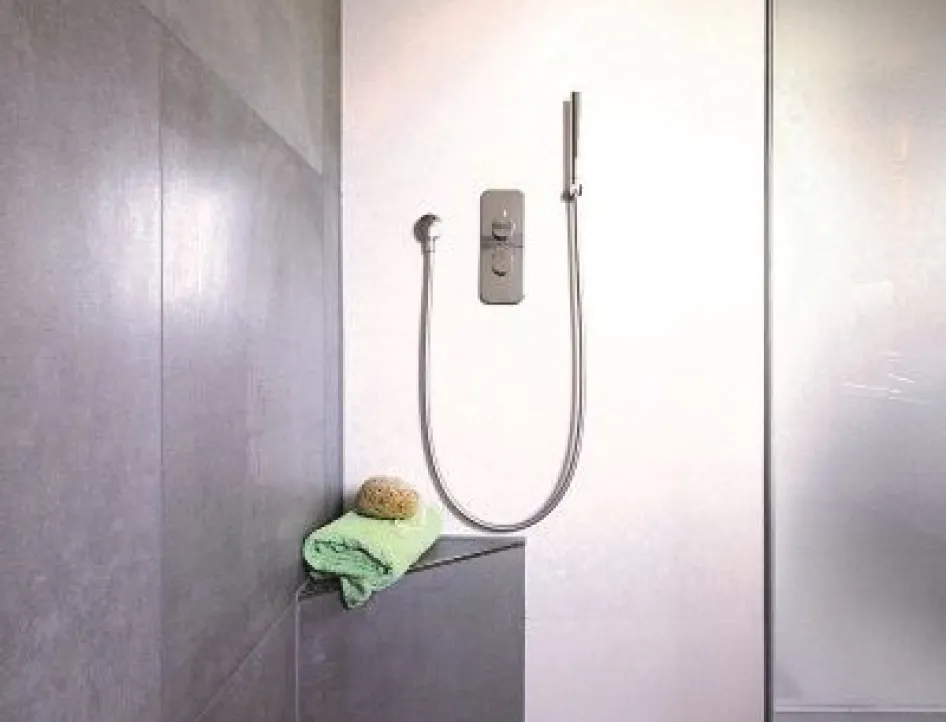 Barrierefreie Dusche mit grauen Fliesen, Sitzbank, Handbrause und Ablage mit Handtuch und Schwamm.