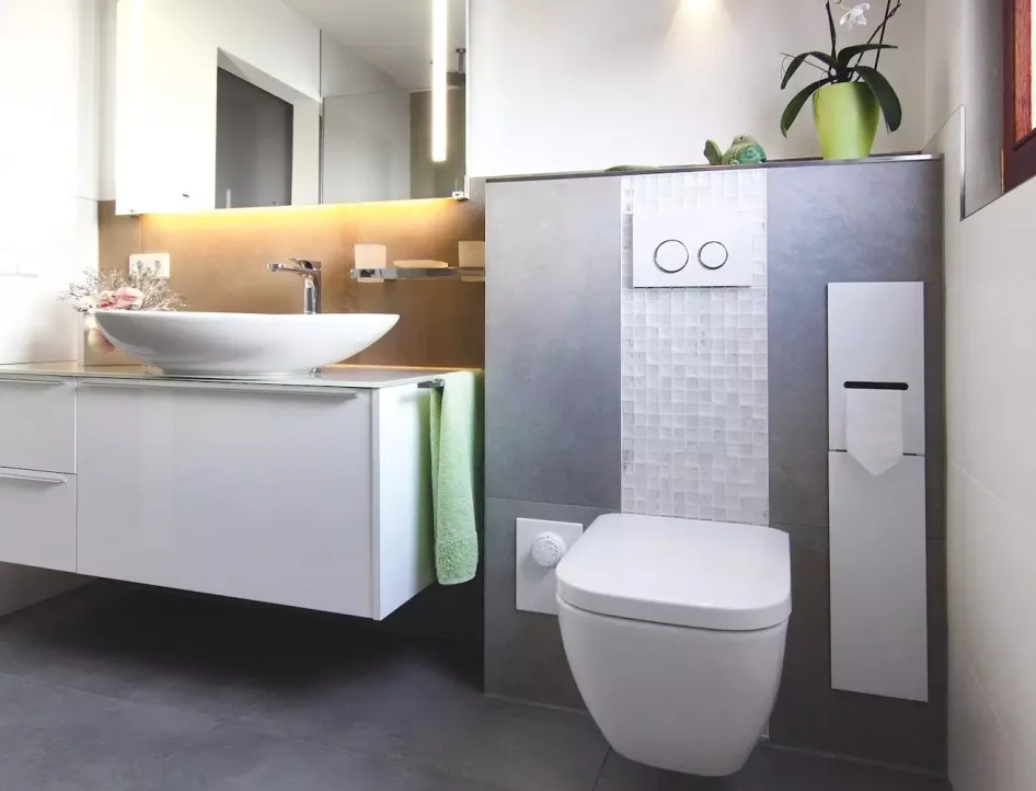 Modernes barrierefreies Badezimmer mit weißem Aufsatzwaschbecken, Wand-WC, beleuchtetem Spiegel und grauen Fliesen.