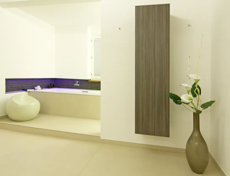 Wellnessbad mit moderner Badewanne, LED-Beleuchtung, Holzschrank und dekorativer Vase mit weißen Blumen.