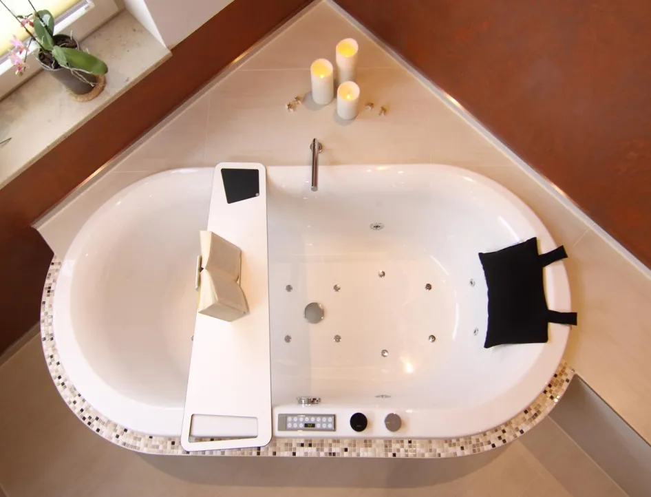 Elegante Whirlpool-Badewanne mit Mosaikfliesen, Ablagebrett mit Buch, schwarzem Kopfkissen und Kerzen zur stimmungsvollen Dekoration.