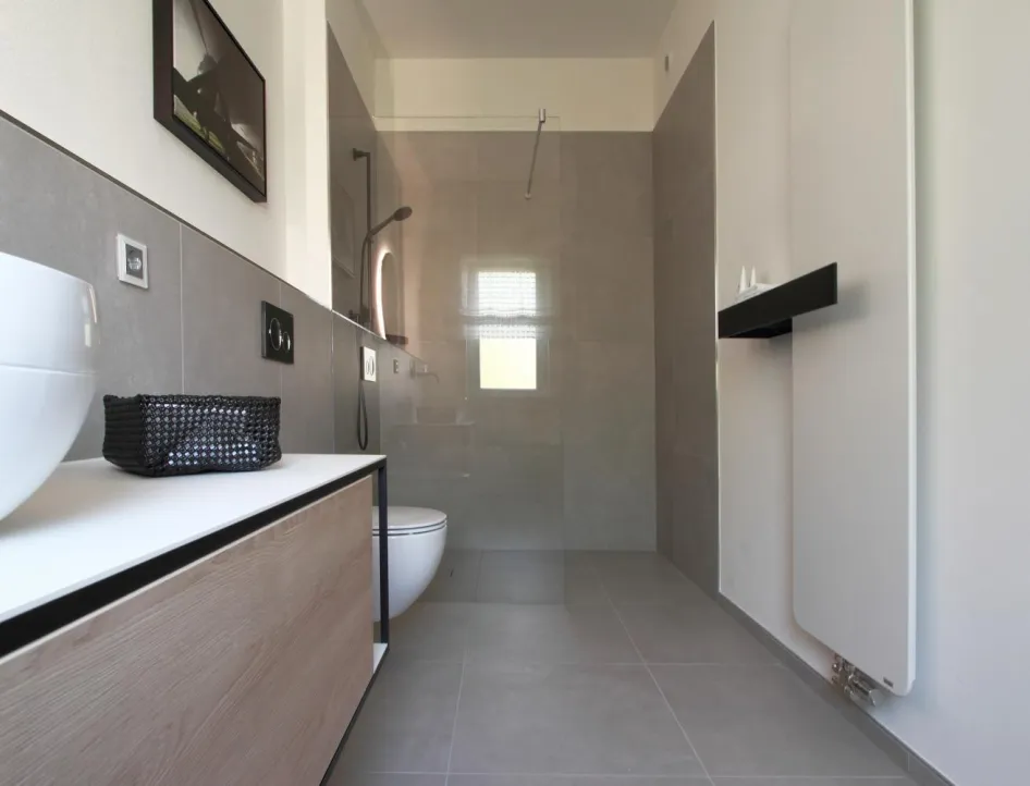 Modernes Gäste-Bad in Betonoptik mit wandhängendem WC, bodengleicher Dusche, Waschtisch mit Holzfront und stilvollem Design-Heizkörper.
