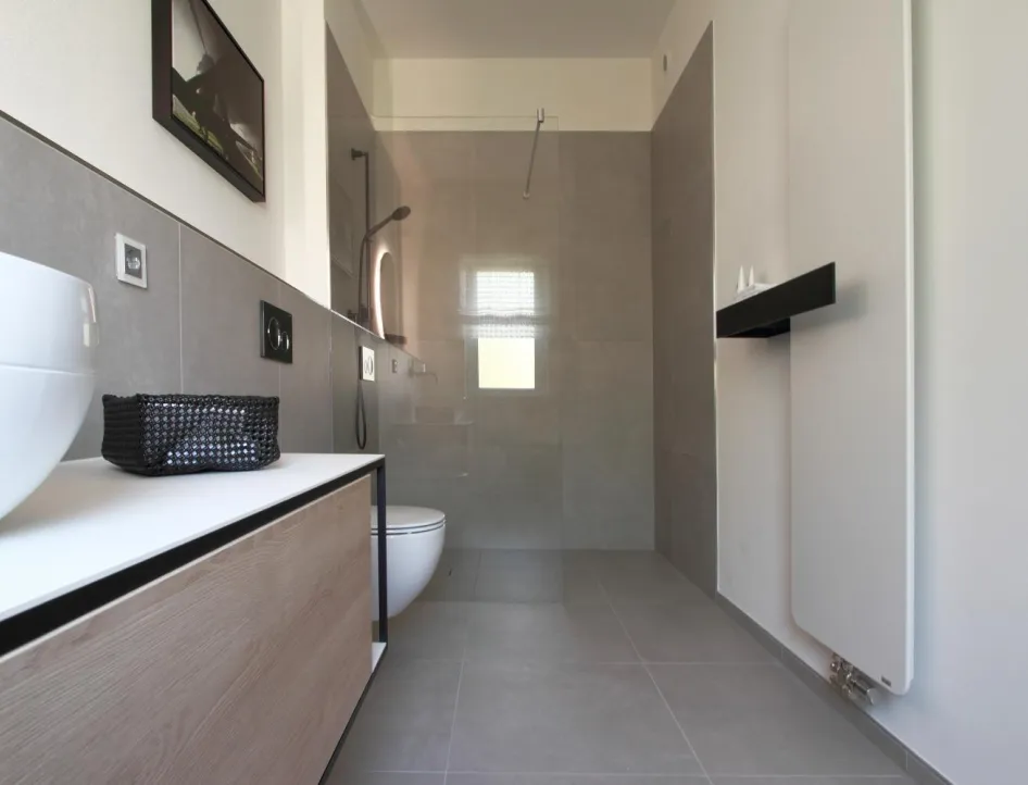 Modernes Gäste-Bad in Betonoptik mit wandhängendem WC, bodengleicher Dusche, Waschtisch mit Holzfront und stilvollem Design-Heizkörper.