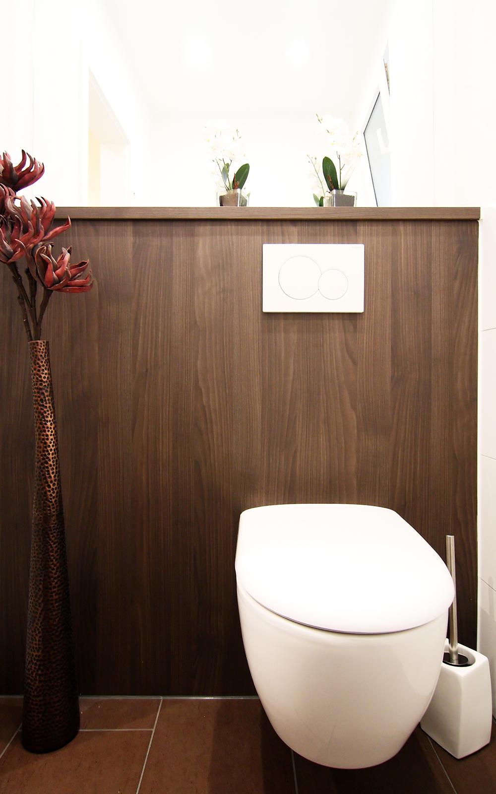 Dunkle Holzverkleidung mit großem Spiegel und weißem Toilettenbecken.