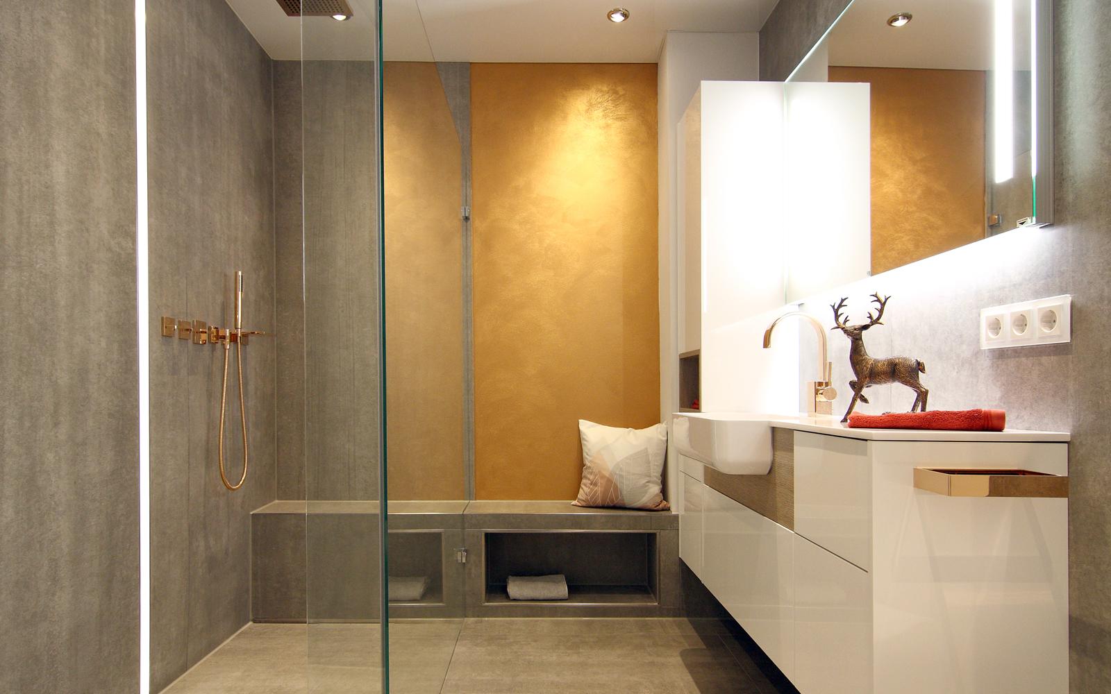 Badezimmer mit Dusche und Waschtisch in Weiß- und Goldtönen.